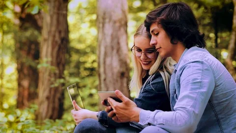 Young Couple Using Laptop And Tablet While Sitting In Forest Video stock 89893455