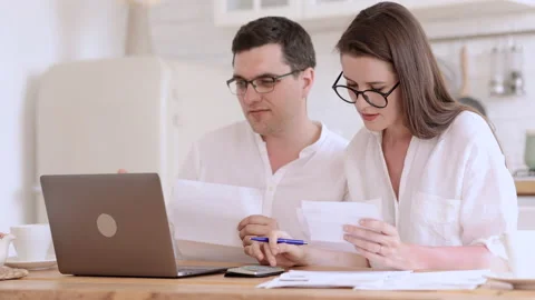 Young couple using laptop and working on paper project while sitting at table in Stock Footage 165792631