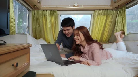 Young couple using laptop computer on bed of a camper RV van motorhome Stock Footage 149312554