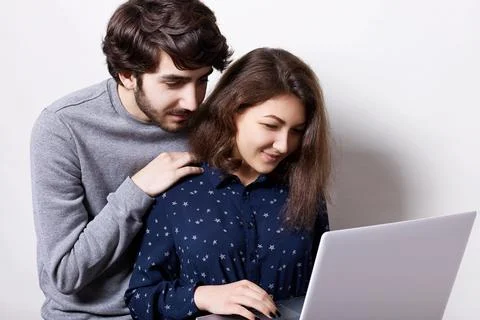 Young couple using laptop computer together. Attractive bearded man dressed i Stock Photos