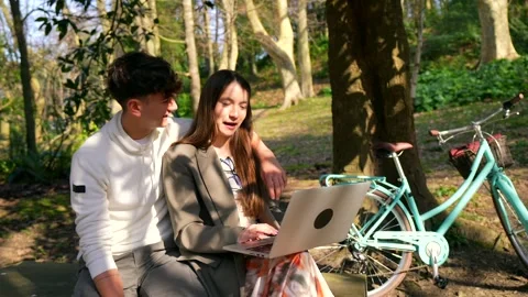 Young couple using laptop in park near bicycle Stock Footage 303484924