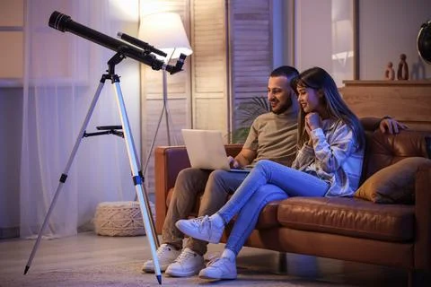 Young couple using laptop on sofa and telescope in room at night Fotos Stock
