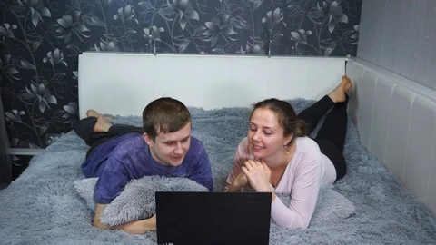 Young couple using a laptop while lying on their bed. Something funny shows the  Stock Footage 99457810