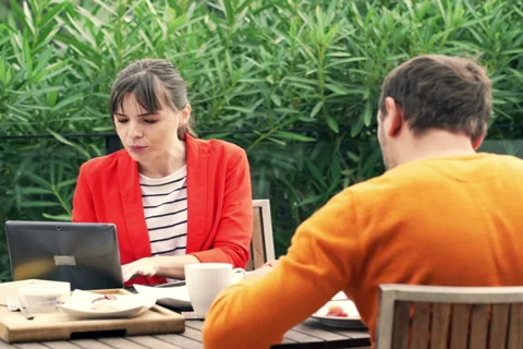 Young couple using modern laptop during breakfast on terrace at home  NTSC Stock Footage 57357314