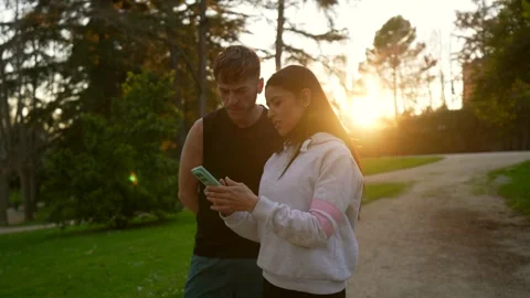 Young couple using navigation app on smartphone at sunset in park Stock Footage 333235186
