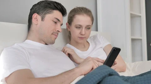 Young Couple Using One Smartphone in Bed Stock Footage 105726529