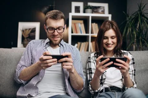Young couple using personal gadgets on couch Stock Photos