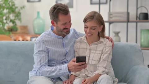 Young Couple Using Phone while Sitting on Sofa at Home Stock Footage 287894585