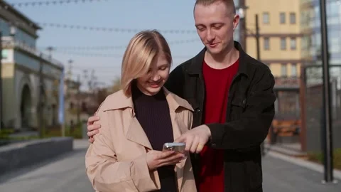 Young Couple Using Smartphone and Walking Down the Street Stock Footage 314631545