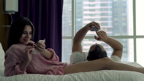 Young couple using smartphone in bedroom with skyscraper view Stock Footage 71989859