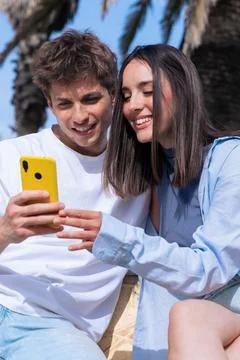 Young couple using smartphone on bench under palm trees smiling at phone social Stock Photos