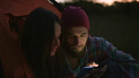 Young couple using a smartphone in the evening near the tent. Vídeo Stock 116557343