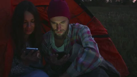 Young couple using a smartphone in the evening near the tent. Vídeo Stock 116926420