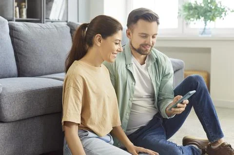 Young couple using smartphone, spending time on internet on weekend at home Stock Photos