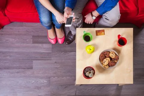 Young couple using smartphone while sitting on couch Stock Photos