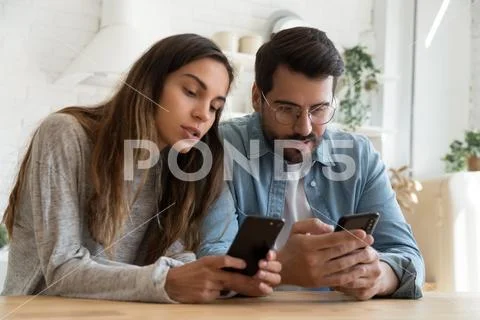 Young couple using smartphones, discussing news, looking at screen Stock Photos