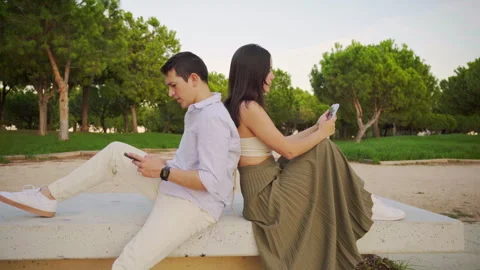 Young couple using smartphones sitting back to back in park Stock Footage 303855161