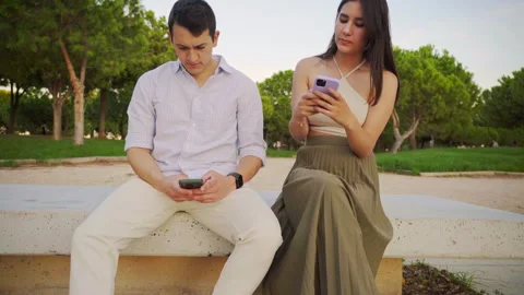 Young couple using smartphones while sitting on bench in park Stock Footage 303854667