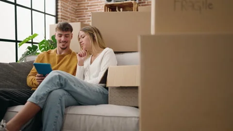 Young couple using touchpad sitting on sofa at new home Video stock 167421091