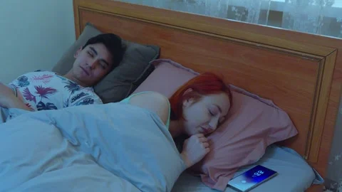 Young Couple Waking Up in Bed as Smartphone Alarm Rings in Morning Stock Footage 345099833
