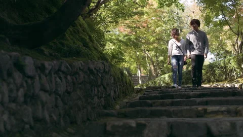 Young couple walking down a stone pathway towards steps under a shaded forest in Stock Footage 199459979