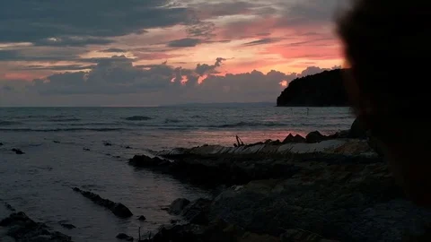 Young couple walking in evening on rocks near shore against a red sunset. Video stock 80165535