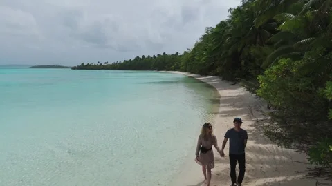 Young couple walking hand in hand on a paradisiacal beach. Aerial backwards shot Stock Footage 297031425