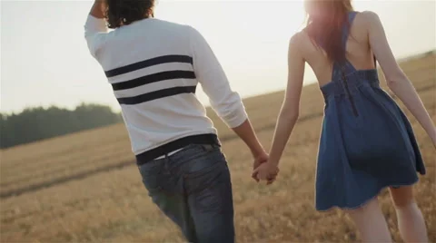 Young couple walking through the field at sunset holding hands Stock Footage 54638063