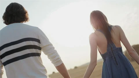 Young couple walking through the field at sunset holding hands. Medium close-up Stock Footage 54638347