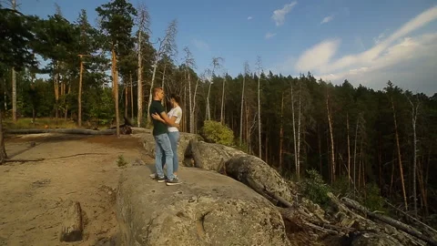 A young couple walks in a pine forest on stone rocks on a bright Sunny day. 스톡 동영상 99012660