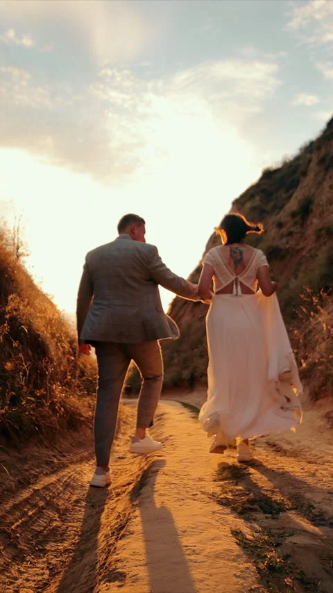 A young couple walks towards the sun between two mountains. Happy people holding Stock Footage 313222829