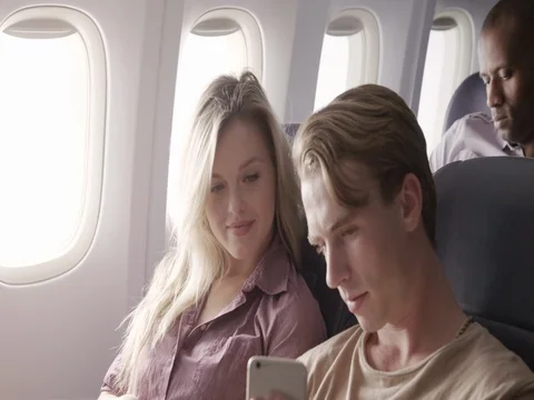Young couple watch content on smart phone while flying on airliner MCU 4K Stock Footage 69735597