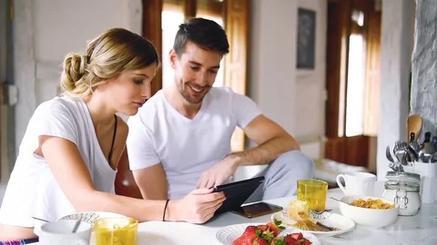 Young couple watching tablet while sitting at table and having breakfast Stock Footage 74727870