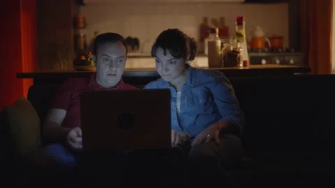 Young couple watching video on the computer at the night lights of their home. Stock Footage 148259012