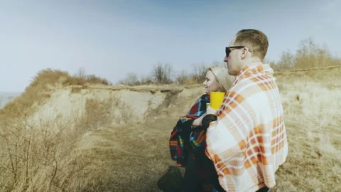 Young couple wrapped in blankets stands on the edge of a cliff near the bank of Stock Footage 87918698