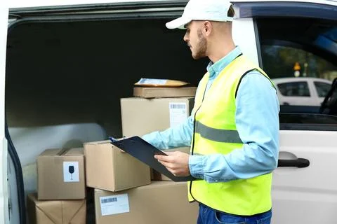Young courier checking amount of parcels in delivery van, outdoors Fotos Stock