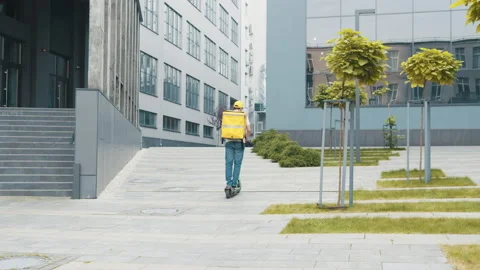 Young courier rides on his e-scooter. Deliver male parcel delivery service guy Video stock 171884123