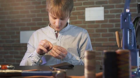 Young craftsman puts in the needle thread to hand sew a DIY product. Stock-Footage 130214368