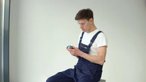 Young craftsman in work uniform and with a screwdriver in his hands sits on a Stock Footage 147040589