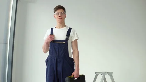 Young craftsman in work uniform and goggles stands on a white wall background Stock Footage 147040661