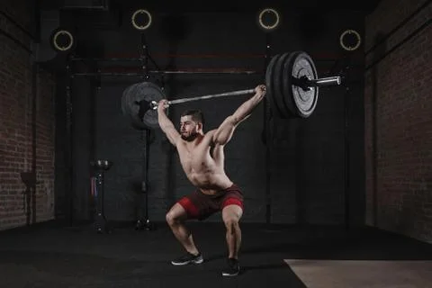 Young crossfit athlete lifting heavy barbell overhead at gym. Handsome ma Stock Photos