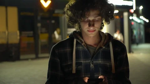 Young curly boy using smartphone outdoors at night, screen light on face, 4k 3 動画素材 95424897