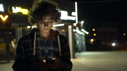 Young curly boy using smartphone outdoors at night, screen light on face, 4k  2 Vidéo 95424929