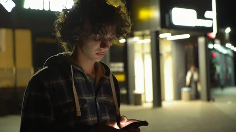 Young curly boy using smartphone outdoors at night, screen light on face, 4k  1 動画素材 95425233