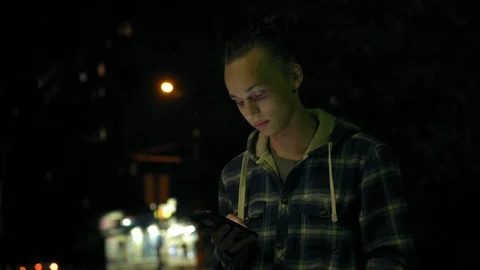Young curly boy using smartphone outdoors at night, screen light on face, 4k 4 Video stock 95425395