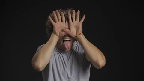 A young curly-haired guy builds faces, fools around. He brings his palms to his Video stock 139473576