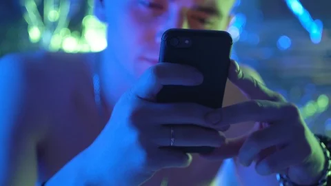 A young, curly-haired guy sits at a table and uses the phone. 库存影片 123574361