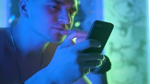 A young, curly-haired guy sits at a table and uses the phone Vidéo 123574517