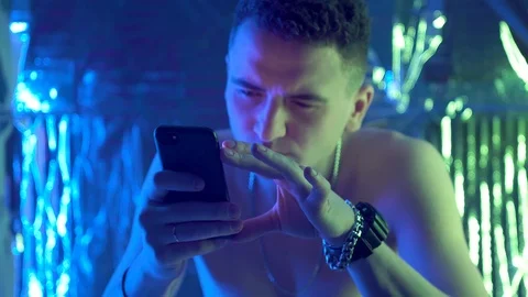 A young, curly-haired guy sits at a table and uses the phone 库存影片 123574821