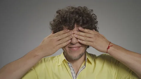 Young curly-haired guy writhes his faces on camera. He closes his eyes with his Stock Footage 139473766